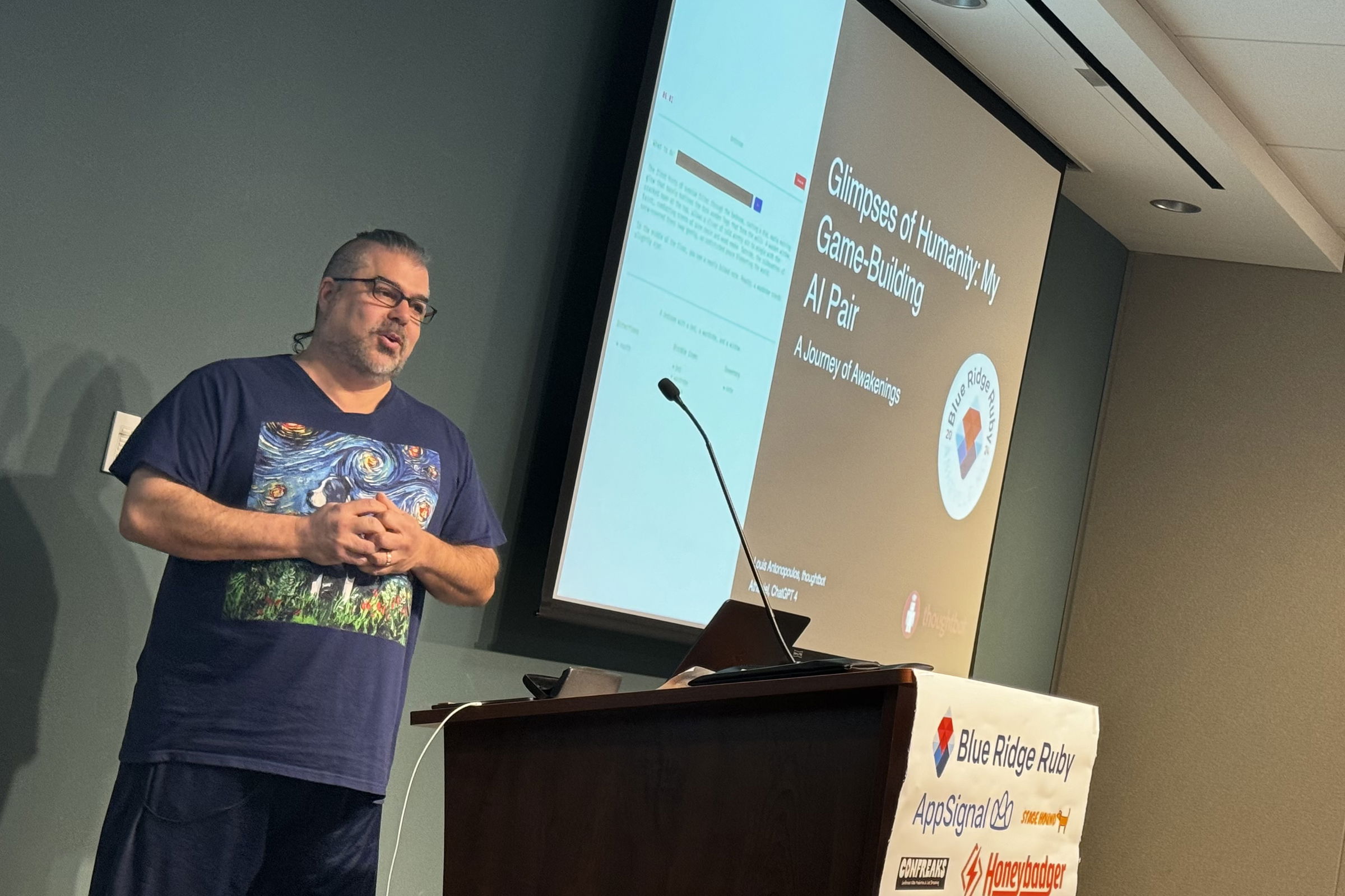 Louis Antonopoulos presents at Blue Ridge Ruby conference on “Glimpses of Humanity: My Game-Building AI Pair,” wearing a shirt with a Van Gogh-inspired design, addressing an audience with a slide displayed behind him.