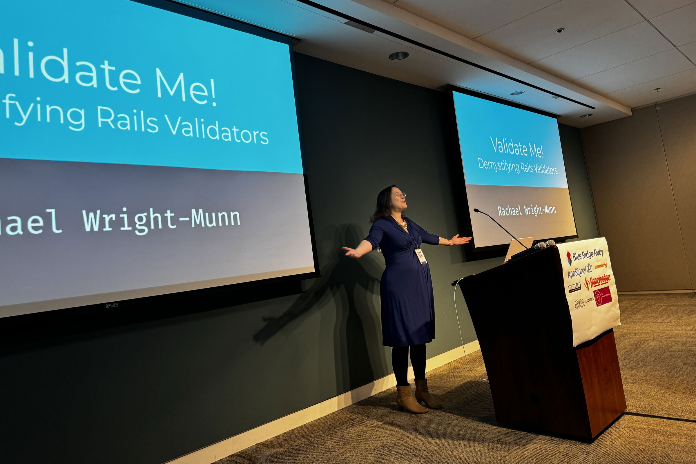 Rachael Wright-Munn presents on “Validate Me! Demystifying Rails Validators” at Blue Ridge Ruby conference, gesturing expressively while addressing the audience, with the presentation title displayed on the screen behind her.