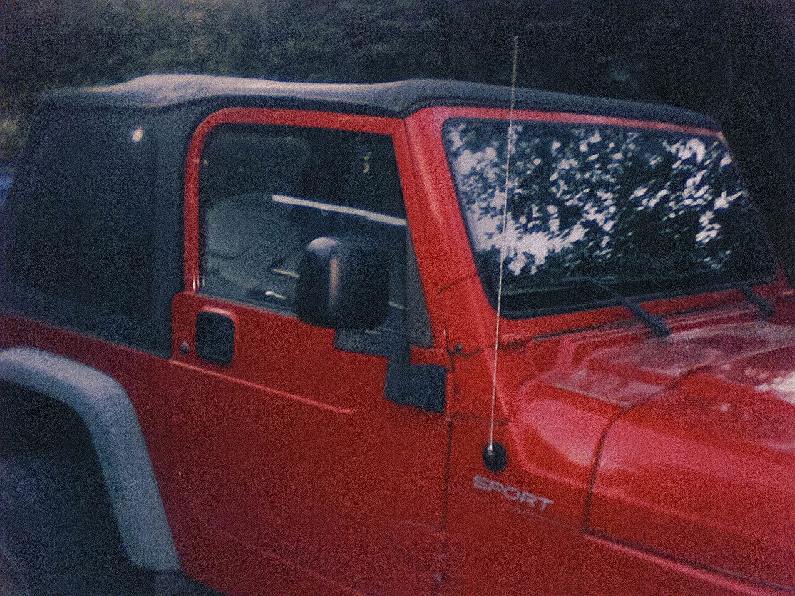 A red Jeep Wrangler Sport with a soft top, parked outdoors.