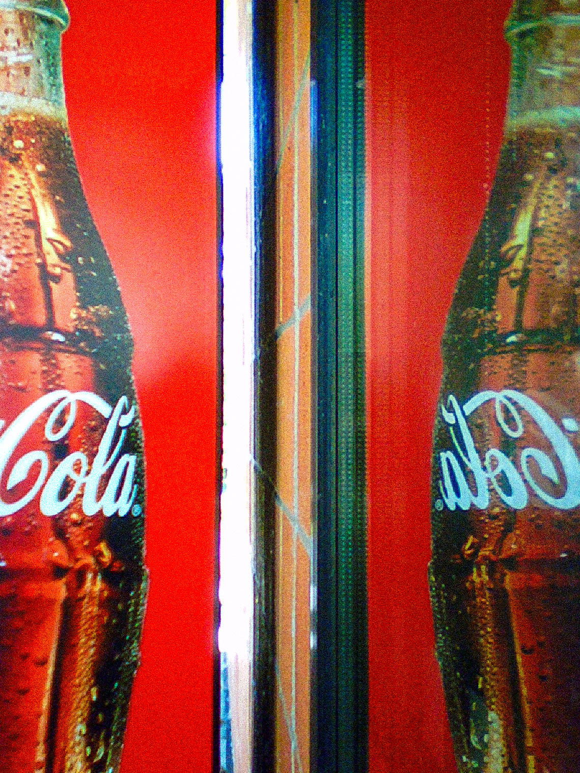 A close-up photo of a Coca-Cola advertisement on a red background, mirrored in a reflective surface.