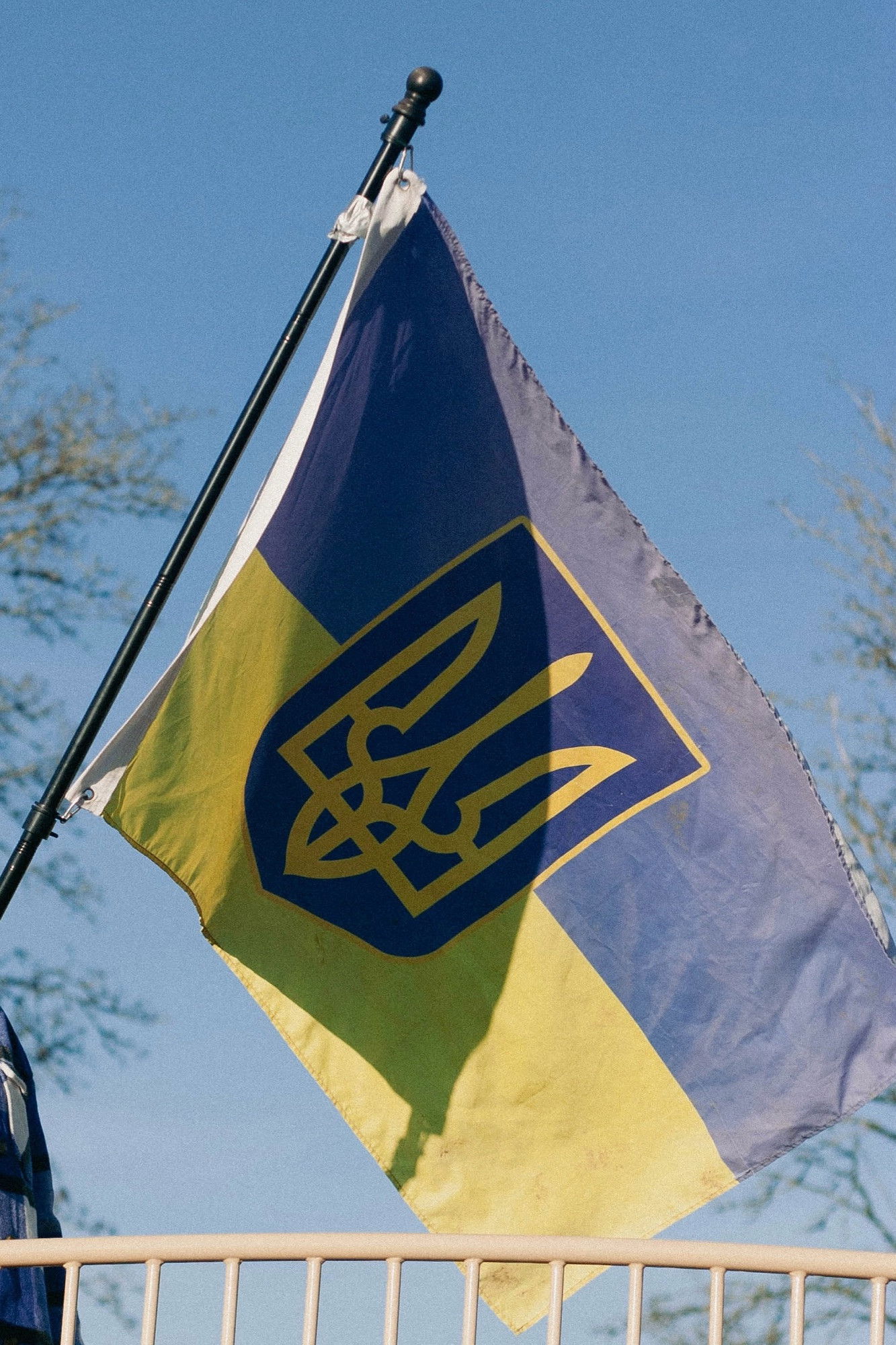 A flag of Ukraine displaying the national trident emblem against a bright blue sky.​​​​​​​​​​​​​​​​