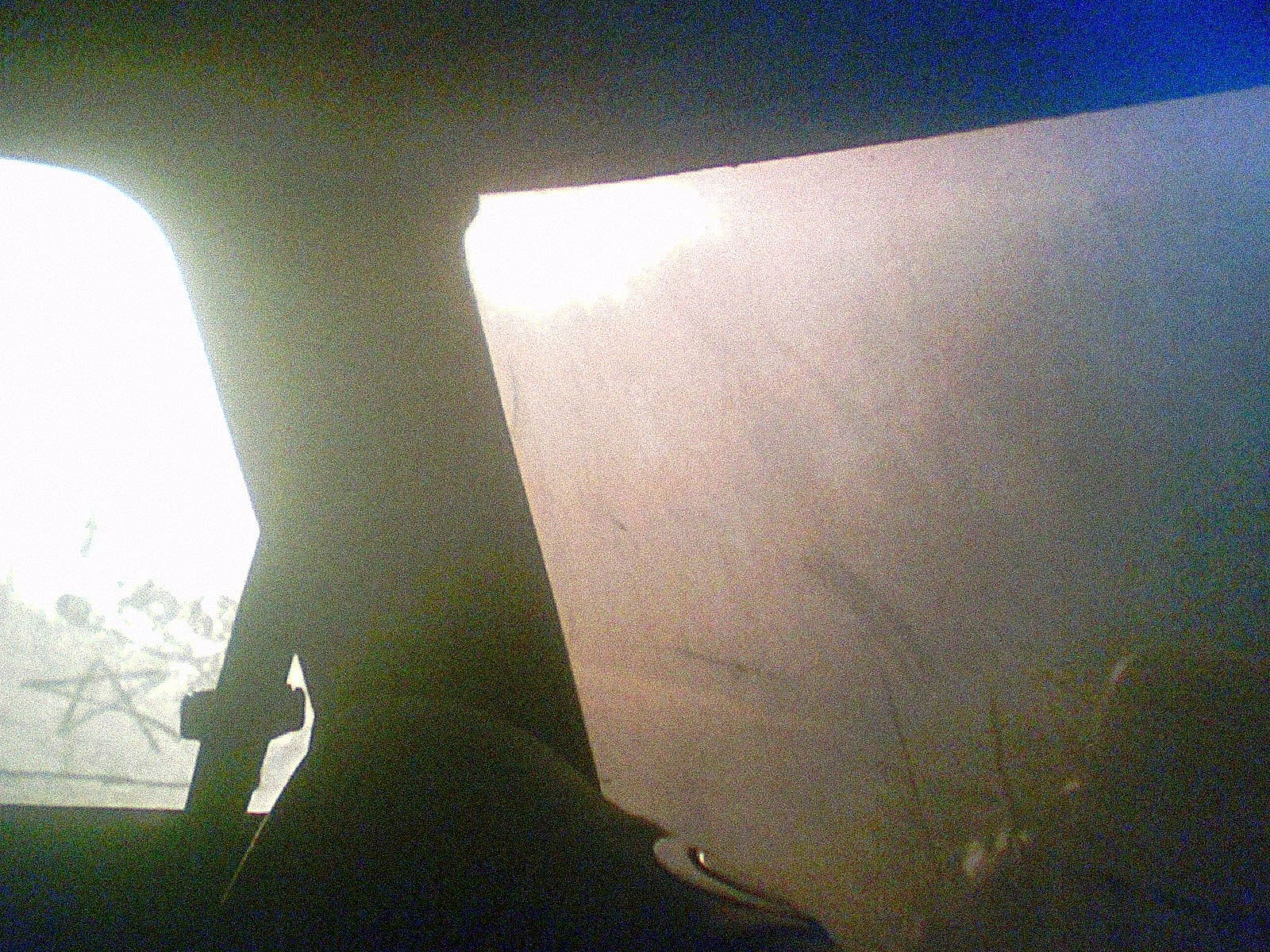 A view from inside a car showing the silhouette of the vehicle's frame dividing two windows, with bright overcast daylight visible through the glass, creating strong contrast between the dark interior and light exterior.