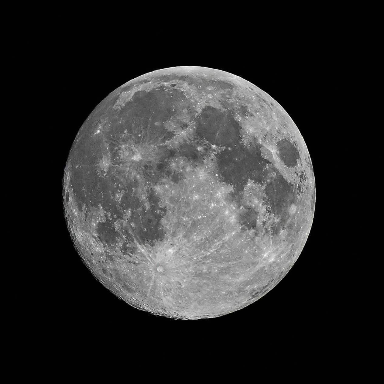 A detailed black and white photograph of a full moon against a black background, showing the moon's complete circular form with its distinctive craters, dark maria regions, and bright highland areas clearly visible across its surface.