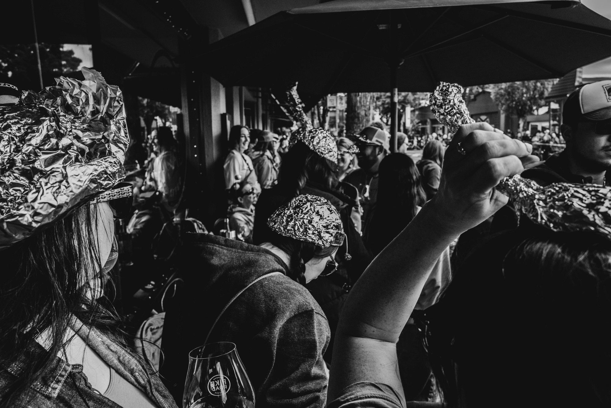 A black and white photo of a group of people at a street festival, many wearing tinfoil hats. 