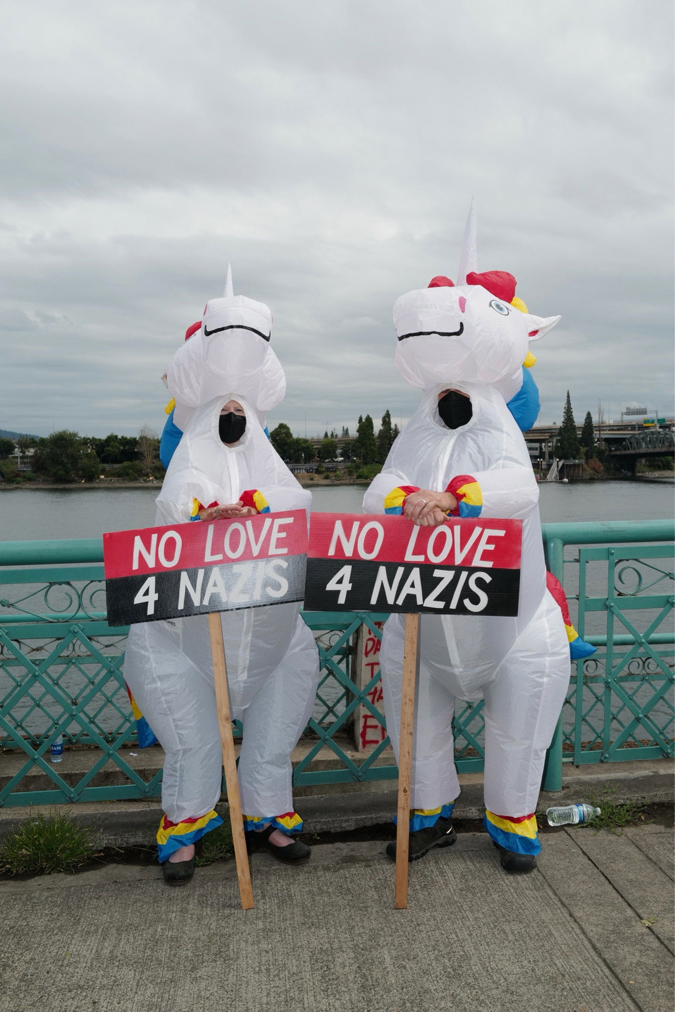 Two people dressed in inflatable unicorn costumes holding signs that read “no love 4 nazis”