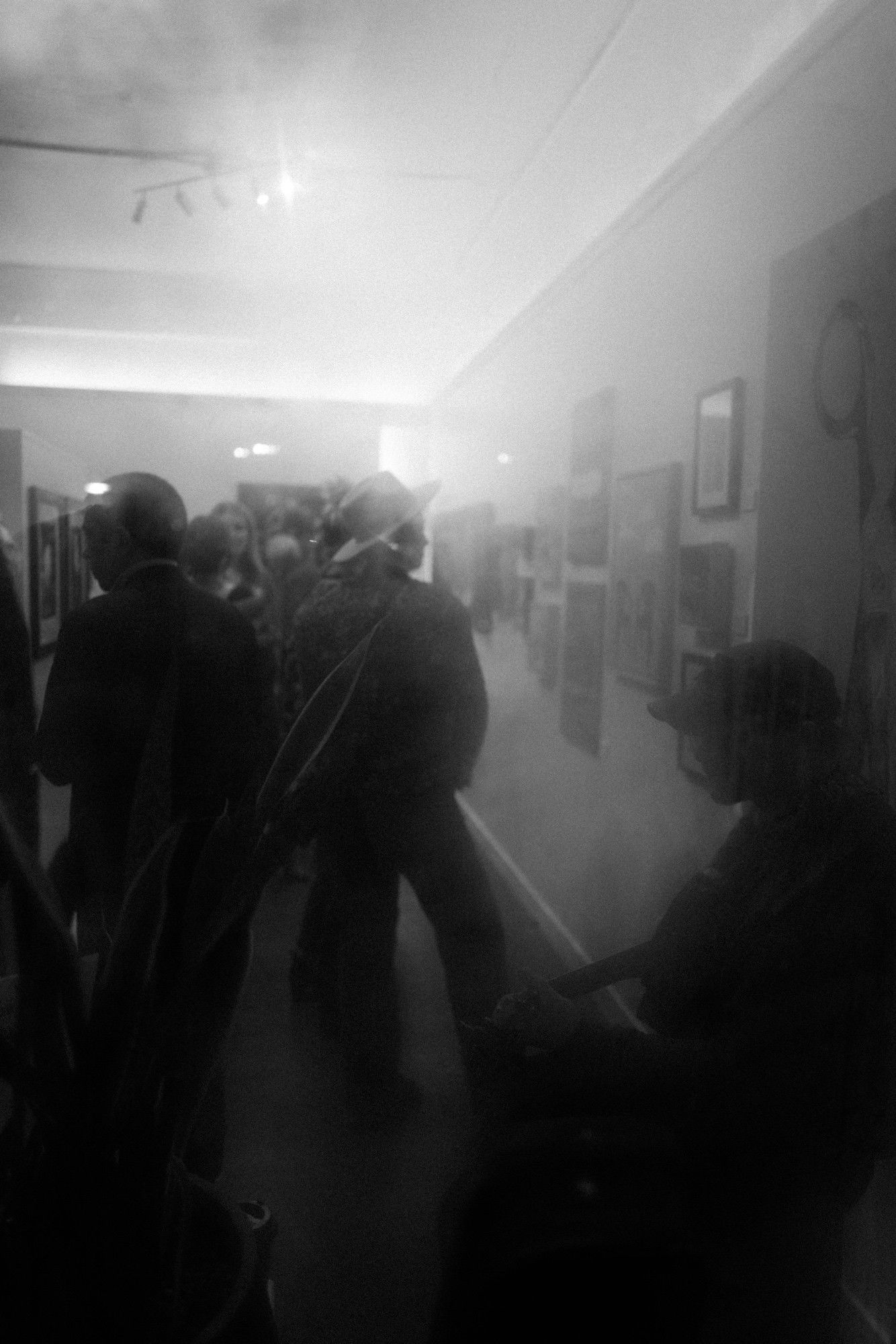 Gallery visitors viewing framed artwork along a corridor, as a musician plays the guitar in the lower right corner.​​​​​​​​​​​​​​​​